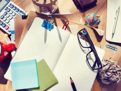 a messy desk with notebooks, glasses, a calculator and other items