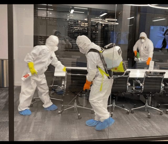 Planned employees in PPE disinfecting an office