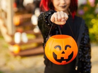 a girl in Halloween costume holding a plastic pumpkin