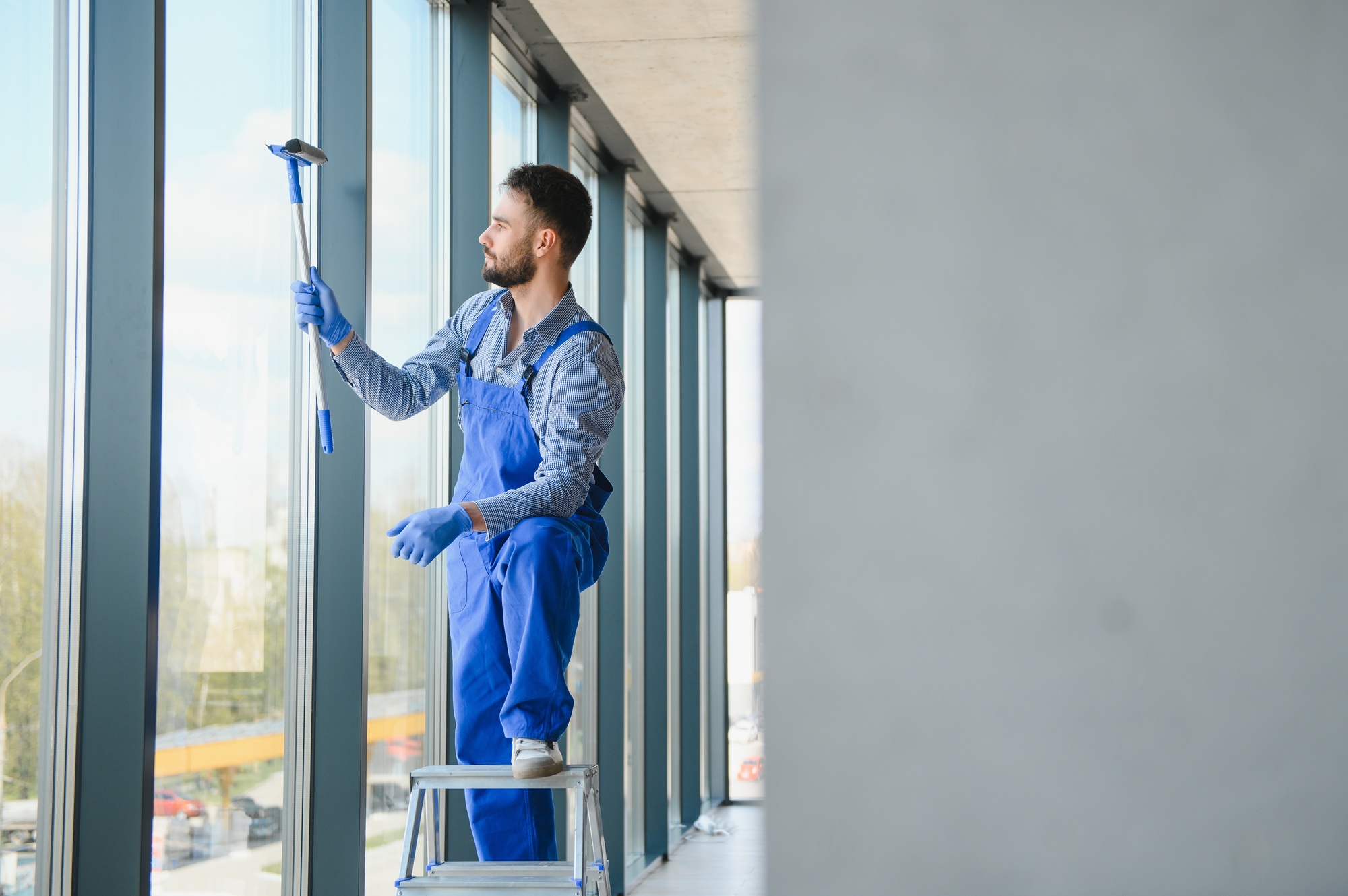 Male janitor cleaning window in office