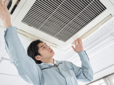 A Japanese male electrician doing maintenance on a commercial air conditioner