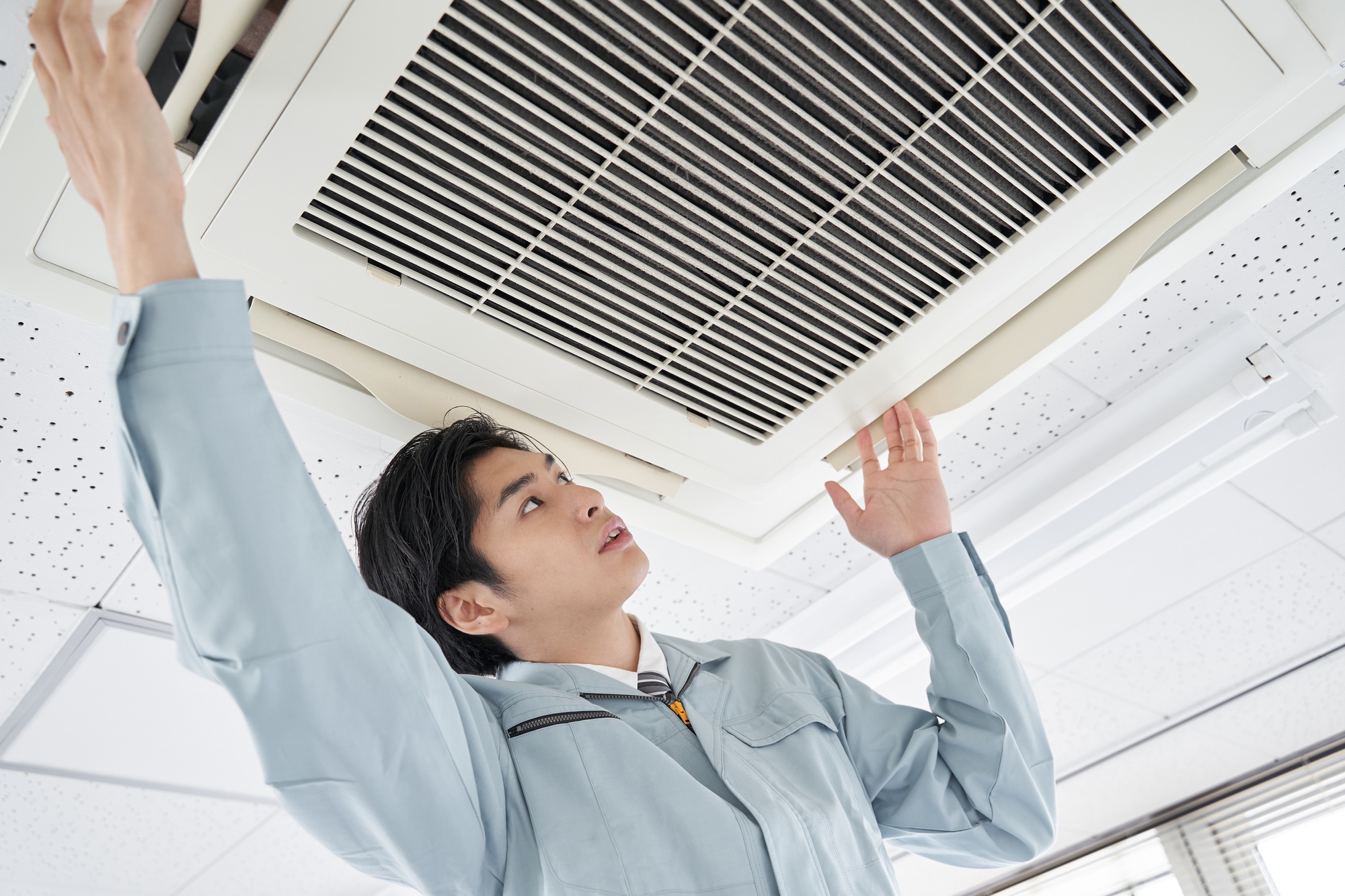 A Japanese male electrician doing maintenance on a commercial air conditioner